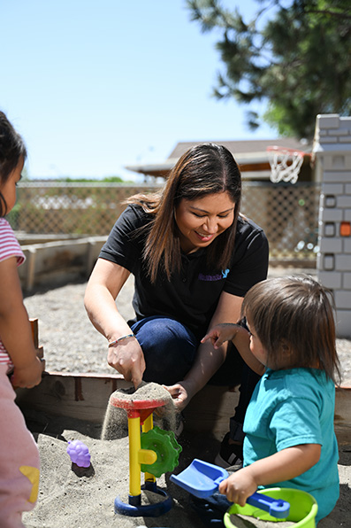 Woman playing in sandbox with children