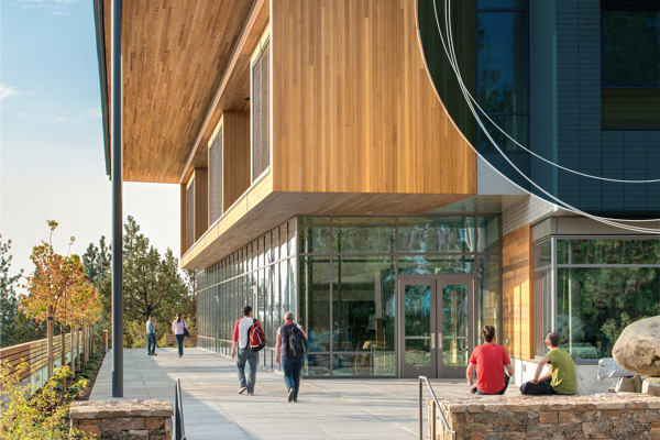Exterior shot of Middleton Science Center. Students sit along raised rock walls around the perimeter of the building on a sunny day.