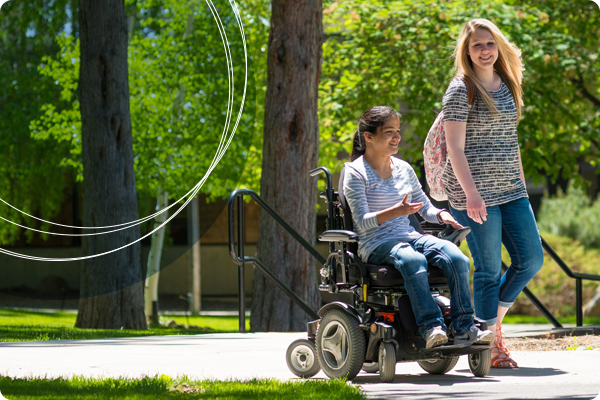 Two Central Oregon Community students moving and talking on sidewalk, one student in an electric wheelchair