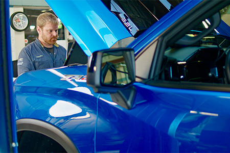 An Automotive Technology student working on a blue vehicle.