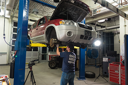 A COCC Automotive student working under a car that's elevated.