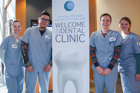 COCC Dental Clinic sign with four students standing beside