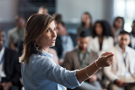 Woman giving economics lecture to diverse business audience