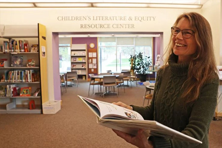 Teacher reading a book in front of the entrance to COCC's Children's Literature & Equity Resource Center (CLERC)