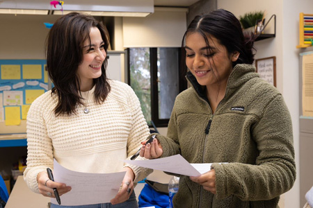 Two female community college education students laughing together and reviewing paperwork