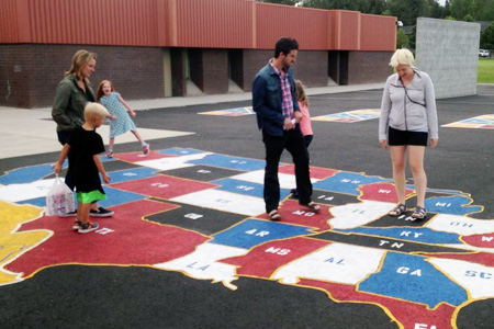 Geography careers - elementary school teachers with students walking on giant asphalt map of the United States