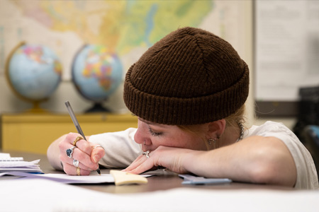 Geography student in geography classroom writing with pen and paper