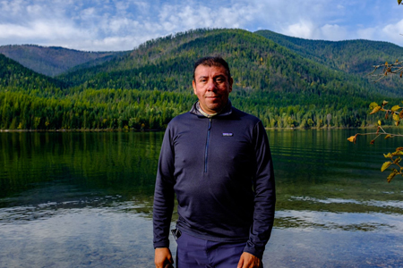 Carlos Vasquez standing in front of a clear lake and forested hills