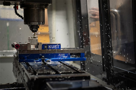 Close-up of a CNC milling machine cutting a metal workpiece, with coolant spraying as the rotating tool shapes the part inside an industrial enclosure.
