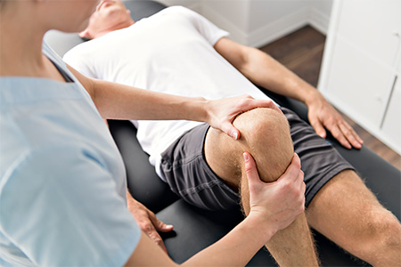 Close up of a man's knee being worked on while he's laying down on a massage table.