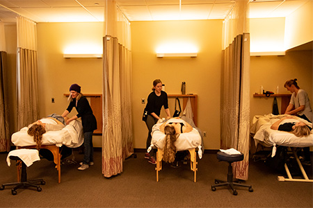 Instructors demonstrating massage techniques on volunteers laying face down on massage tables.