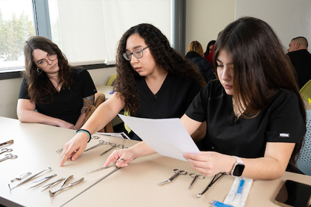 Three medical assisting students looking over table of medical instruments