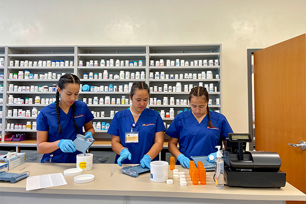 Three Pharmacy Tech students work in a simulated pharmacy lab.
