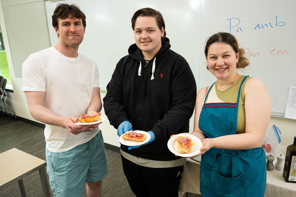 Three world language students holding plates of food